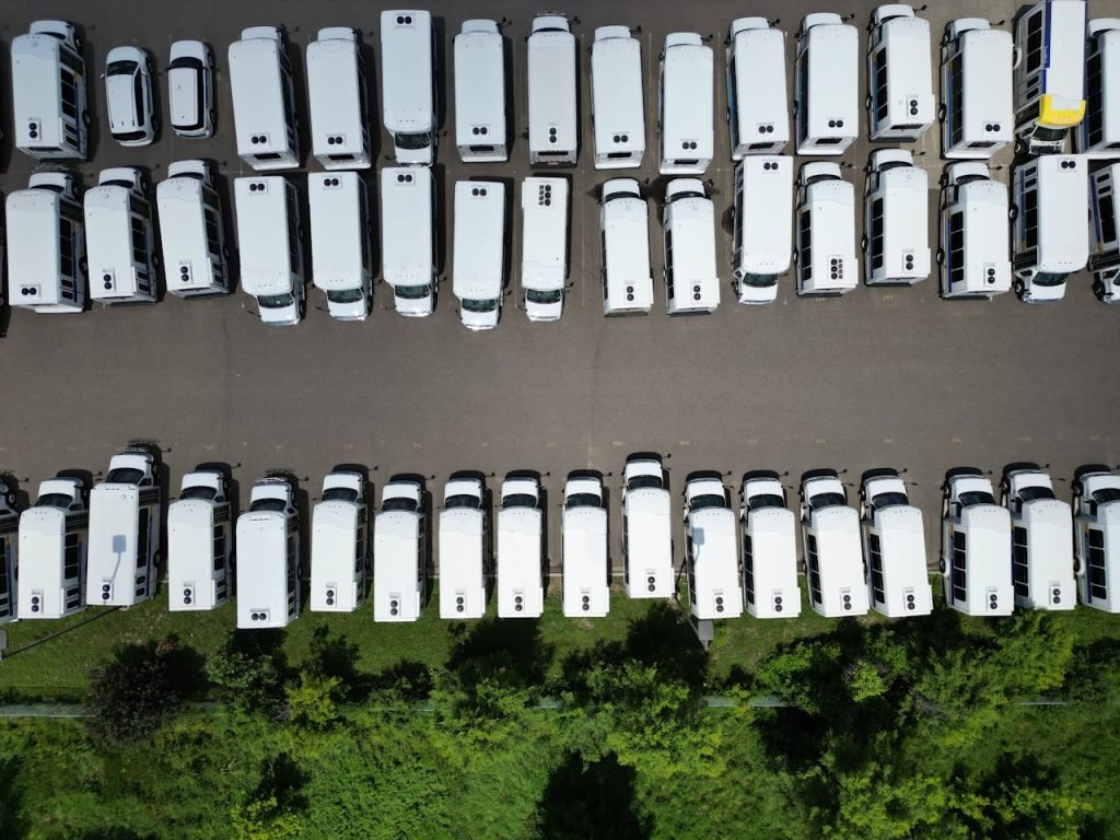 Aerial view of a large parking lot filled with white vans on a sunny day.