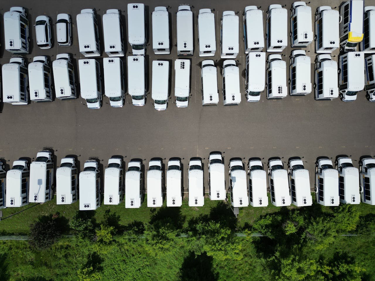 Aerial view of a large parking lot filled with white vans on a sunny day.