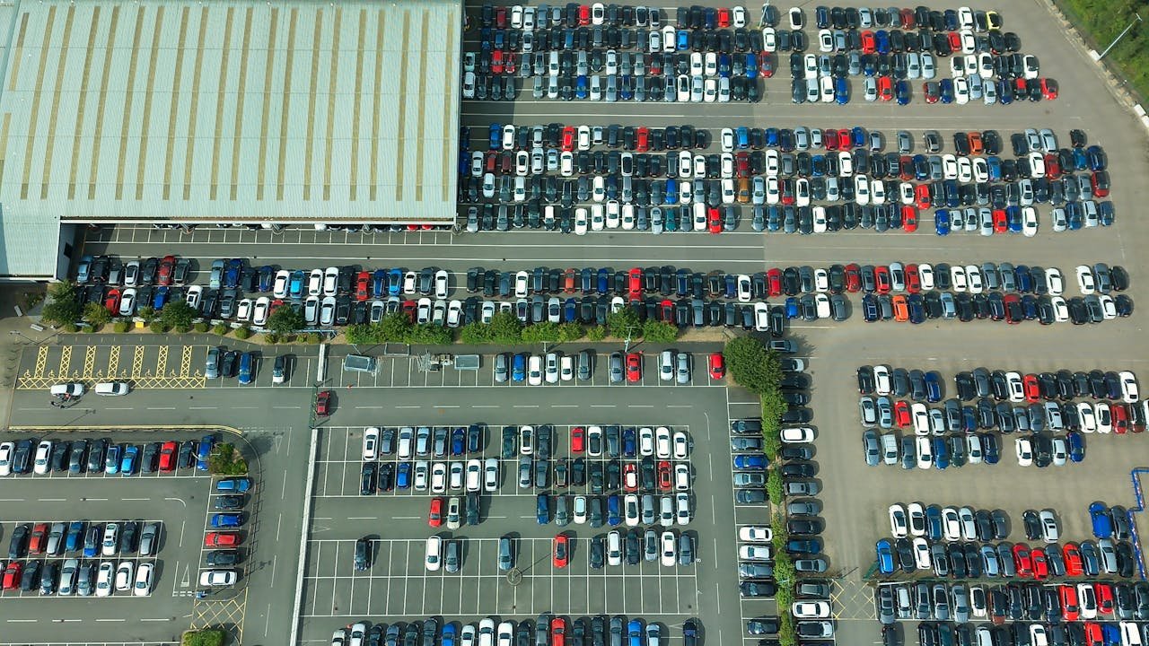 Aerial shot of a vast parking lot filled with parked vehicles and a large building.